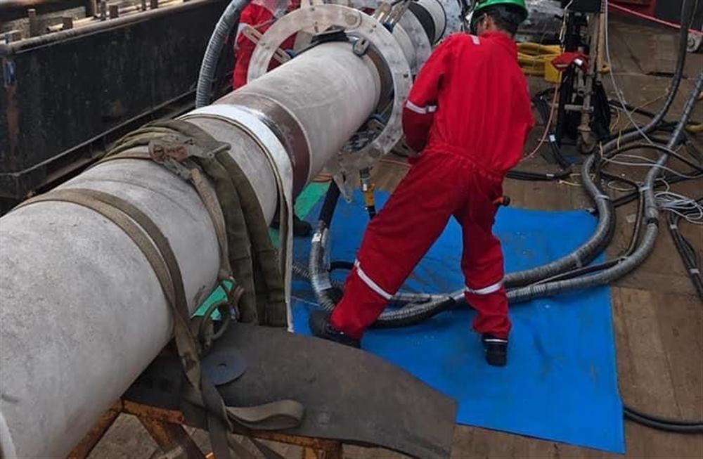 Technician in red coveralls installing marine cable/pipe equipment on a vessel deck